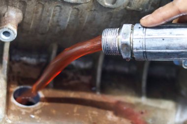 Bir tamirci metalik bir motora ya da dişli kutusuna doldurma başlığı kullanarak parlak kırmızı şanzıman sıvısı döküyor.