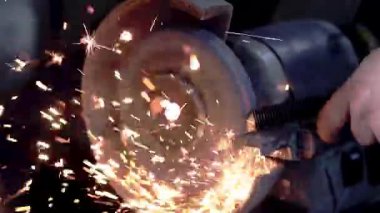 Hareket halindeki bir bank öğütücüsünün yakın çekimi, metal bir çubuğu bilemek ve karanlık mekanik bir ortamda parlak turuncu kıvılcımlar ve ışık yağmuru yaratmak..