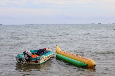 16 Kasım 2025 'te Balikpapan-Endonezya' da küçük motorlu bir tekne sakin denizde sarı ve yeşil şişirilebilir bir muz teknesinin yanına demirlemiş ve su sporu faaliyetlerine hazırdır..