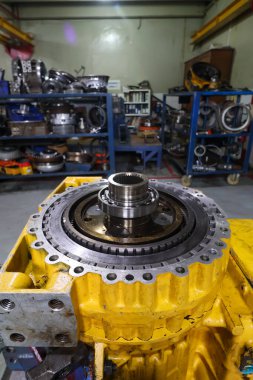 Parçalanmış ağır makine nakil bileşeni, canlı sarı bir kaplama üzerine monte edilmiş vites ve yataklar, bir atölyede bakım veya onarım için hazır.