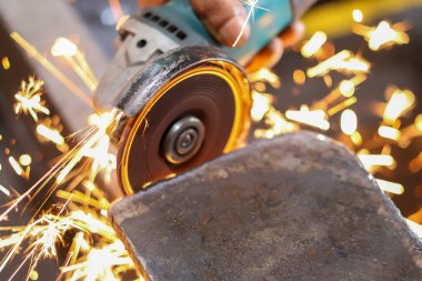 Açı öğütücüsünün yakın çekimi metali kesiyor, parlak sarı ve turuncu kıvılcımlar üretiyor, ağır üretimi ve metal işçiliğini sembolize ediyor.