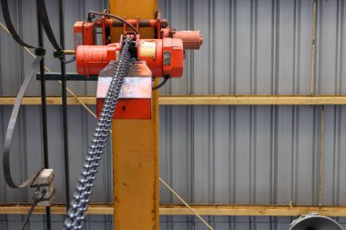 Düşük açılı sanayi kırmızı zinciri (tepe üstü vinç) bir fabrika veya depoda sarı dikey çelik kirişe monte ederek ağır kaldırma ekipmanları ve endüstriyel inşaatı vurguluyor..