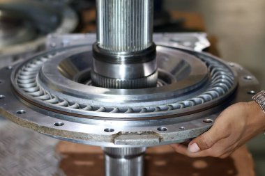 Bir işçinin elinin, montaj sırasında serinletici bir yüzgeç yapısına sahip büyük, parlak metalik bir bileşeni tutarken yakın plan görüntüsü..