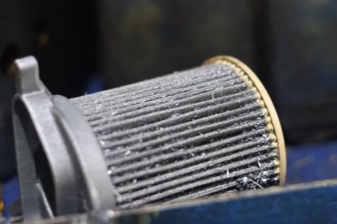 Yoğun kirlenmiş, metalik motor yağı ya da yakıt filtresi elementinin kapana kısılmış metal talaşlı, atölye tezgahında dinlenen, aşınma, onarım ve otomotiv bakımı öneren yakın plan.