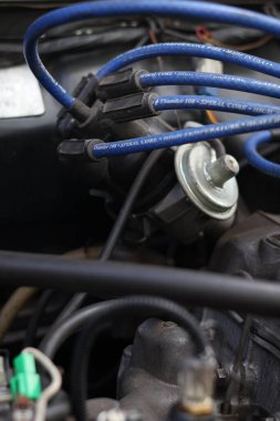 Balikpapan-Endonezya Desember 08, 2025 Mavi yüksek performanslı buji kabloları klasik bir içten yanmalı motorun koyu renk dağıtım kapağına bağlı, otomotiv ateşleme sistemini gösteriyor.