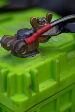 Kirli, korozyonla kaplı, parlak yeşil bir araba aküsünün kablosu kanat fındığıyla korunmuş, son durağının yakın çekimi..