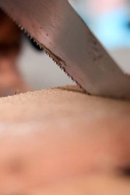 Tahta yığınını kesmek için parlak yeşil saplı bir el testeresi kullanan birinin yakın plan fotoğrafı. Kesme eylemine ve alete odaklan.