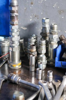 Çeşitli metal hidrolik bağlantıların toplanması, hızlı bağlantıların kesilmesi, ve makine atölyesinde bir çalışma tezgahında düzenlenmiş soket anahtarı..