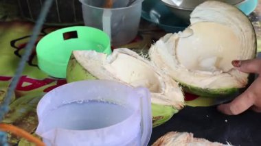 Metal bir kaşık kullanarak ellerinizi yakın plan çekin. Yarısı taze hindistan cevizinden taze beyaz et kazıyın. Geleneksel tropikal meyve içeceği hazırlığı..