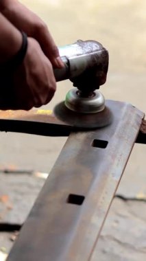 Bir atölyede paslı metal yüzeyi, profesyonel metal bitirme ve restorasyon işlemini düzeltmek için hava açısı zımpara makinesi kullanan bir işçinin ellerine yakın çekim.