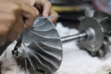 Bir teknisyenin ellerini bir turbo türbin tekerleği, profesyonel metal işçiliği ve mekanik motor onarım servisi için manüel dengeleme hassas bir dosya kullanarak kapat.