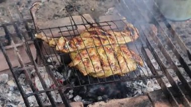 Geleneksel baharatlarla terbiye edilmiş ızgara tavuk, sıcak kömürle pişiriliyor kırsal bir mangal ızgarasında, dumanla ve parlayan közle.