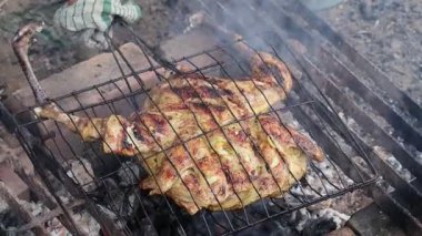 Geleneksel baharatlarla terbiye edilmiş ızgara tavuk, sıcak kömürle pişiriliyor kırsal bir mangal ızgarasında, dumanla ve parlayan közle.