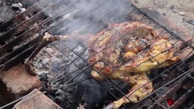 Geleneksel baharatlarla terbiye edilmiş ızgara tavuk, sıcak kömürle pişiriliyor kırsal bir mangal ızgarasında, dumanla ve parlayan közle.