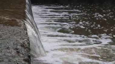 Beton bir çıkıntının üzerinden akan suyun yakın çekimi nehirde köpük ve kabarcıklarla dolu küçük bir şelale oluşturuyor.