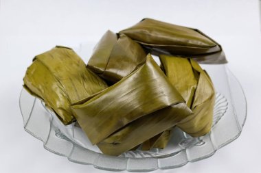 Geleneksel Endonezya muz keki Nagasari muz yapraklarına sarılı beyaz arka planda izole edilmiş bir tabakta servis ediliyor.