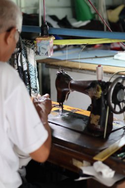 Balikpapan-Endonezya 07 Şubat 2026 Klasik klasik klasik bir dikiş makinesi üzerinde çalışan yaşlı bir terzi basit bir asılı ampul altında.