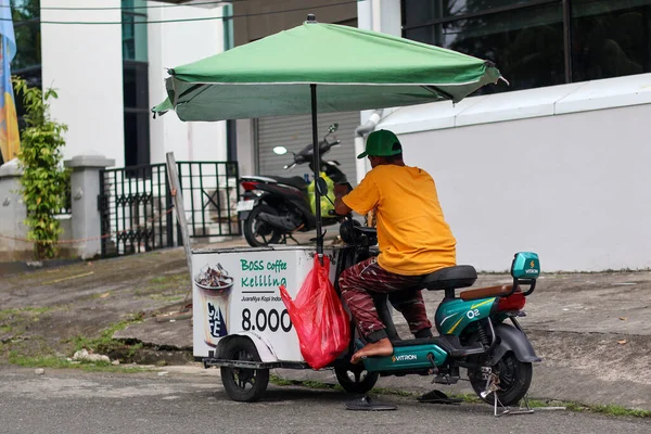 Endonezya-Balikpapan-Endonezya 7 Şubat 2026 Mobil kahve satıcısı yeşil elektrikli scooter ve büyük bir şemsiyeyle Endonezya 'da buzlu kahve satıyor..