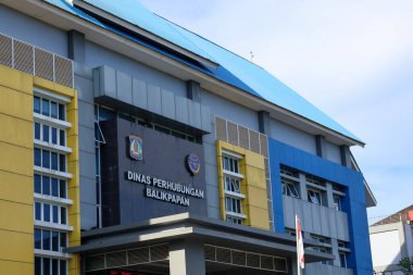 Endonezya-Balikpapan-Endonezya 05 Şubat 2026 Balikpapan Endonezya Ulaştırma Bakanlığı modern hükümet binası mavi ve sarı ön cephe tasarımı açık mavi gökyüzü altında park etmiş arabaların önünde.
