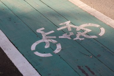Yeşil asfalt bir bisiklet yoluna asfalt bir bisiklet sembolü çizilmiş. Yıpranmış dokusu ve şehir sokaklarında güneş ışığı gölgeleri var..
