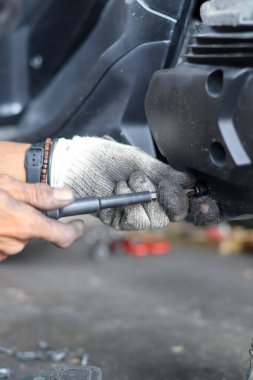 Garajdaki motosiklet motorunu tamir etmek için tornavida kullanan eldiven takan tamircinin fotoğrafını çek..