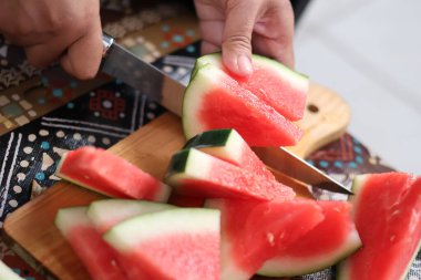 Keskin bir bıçakla ellerini kapat ve taze kırmızı karpuzu tahta bir kesme tahtasının üzerinde üç parçaya ayır. Mutfakta sağlıklı bir organik atıştırmalık hazırla..