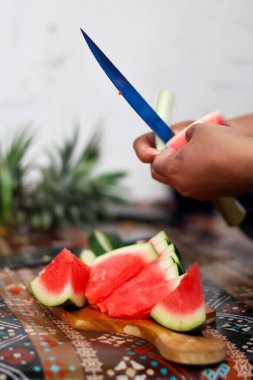 Ellerinizi keskin bir bıçakla kapatın. Olgunlaşmış kırmızı karpuz dilimini dikkatlice soyun. Mutfakta taze organik meyve atıştırmalıkları hazırlayın..