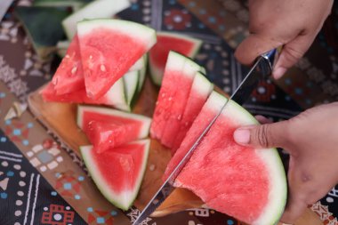 Keskin bir bıçakla ellerini kapat ve taze kırmızı karpuzu tahta bir kesme tahtasının üzerinde üç parçaya ayır. Mutfakta sağlıklı bir organik atıştırmalık hazırla..