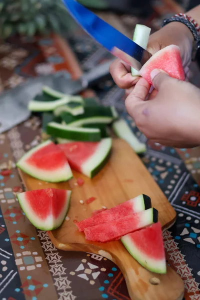 Ellerinizi keskin bir bıçakla kapatın. Olgunlaşmış kırmızı karpuz dilimini dikkatlice soyun. Mutfakta taze organik meyve atıştırmalıkları hazırlayın..