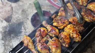 Bir insan kömür ızgarasında terbiye edilmiş balık pişiriyor. Geleneksel bir yaprak fırçası kullanıyor. Mükemmel dumanlı, kömürleşmiş bir doku ve lezzetli bir aroma yaratmak için baharatları dikkatlice uyguluyor..