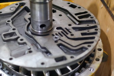 Bir atölyede mekanik onarım sırasında merkezi çelik şaft ve teçhizatla parçalanmış otomatik şanzıman gövdesine yakın çekim..