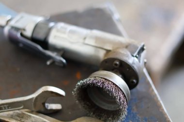 Pnömatik hava açı öğütücüsüne çelik tel bardak fırçası monte edilmiş bir atölyedeki metal tezgah, pas çıkarmak ve endüstriyel yüzeyleri temizlemek için kullanılır..