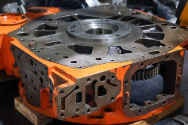 Ağır turuncu Allison şanzıman konutları profesyonel bir atölyede bir çalışma tezgahına yerleştirilmiş. Büyük araç vites kutusu tamiri için sağlam endüstriyel metalik döküm gösteriyor..