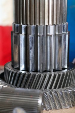 Makine montajı ve makine mühendisliği onarımı için bir imalat atölyesine yerleştirilmiş parlak endüstriyel çelik dişliler ve serpilmiş şaft parçaları..