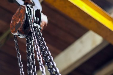 Endüstriyel bir depoda donanım bakımı için kullanılan sarı bir çelik kirişe asılı ağır görev zinciri makarasını kapatın.