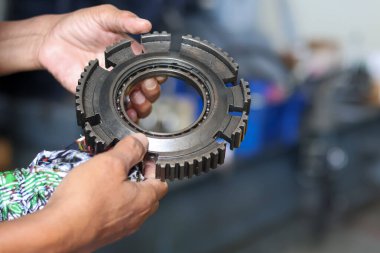 Hasarlı, yağlı metal şanzıman teçhizatını tamir atölyesindeki ağır mekanik yıpranma ve arızaları analiz etmek için inceleyen bir tamircinin eline yakın plan..