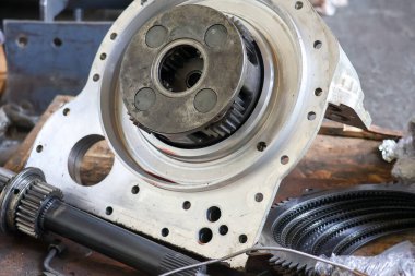 Metal bir konutun içinde ağır bir gezegen teçhizatı montajı, atölye masasındaki endüstriyel mekanik nakil bileşenlerini gösteriyor..