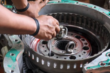 Profesyonel bir tamirci, bir makine onarım işlemi sırasında fabrika atölyesinde hassas bir alet kullanarak ağır bir vites takımını metal bir konuta dikkatlice monte ediyor..