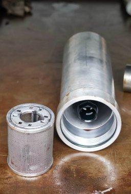 Metalik hidrolik yağ filtresi ve silindirik alüminyum konutları endüstriyel makine hizmetleri sırasında bakım ve yenileme için bir mekanik atölyede bir çalışma tezgahına yerleştirilir..