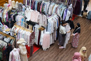 Balikpapan-Endonezya 15 Mart 2026 Alışverişçiler kalabalık bir perakende pazarında renkli Müslüman modası ve geleneksel kıyafetlerden oluşan geniş bir yelpazeye bakıyorlar. Mevsimlik bir satış sırasında bir giysi sergisinin yüksek açılı görüntüsü.