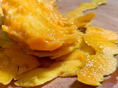 Close-up of juicy mango seed with orange flesh and peels on wooden cutting board, showing freshness and natural texture. Perfect for organic food, tropical, and healthy lifestyle concepts.