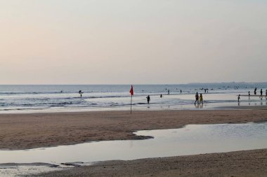 Kuta Sahili 'nin geniş kıyı manzarası yumuşak günbatımı ışığı, sığ su yansımaları, hafif dalgalar ve kırmızı güvenlik bayrağı. Seyahat, doğa, manzara yaz teması için sakin bir hava. 11 Eylül 2025 - Endonezya