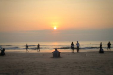 Endonezya, Bali 'deki Kuta Sahili' nde gün batımı görüntüsünde okyanus kenarında insan siluetleri var. Sıcak altın renkler ve sakin atmosfer, seyahat, yaz, rahatlama, duygusal ve yaşam tarzı görselleri için ideal.