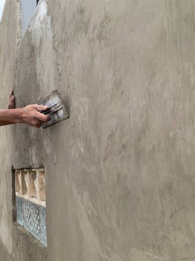 İşçi beton bir duvara beton sıva uyguluyor. Yüzey açılı, yüzeysel bir bakış açısı var. İşçiliği ve ilerlemeyi gösteriyor. İnşaat, yenileme, emlak ve inşaat süreci temaları için ideal.
