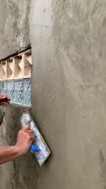 İnşaat işçisi bir mala kullanarak beton duvarları düzleştiriyor. Düşük açı dokuyu ve odaklanmayı gösteriyor, sakin ve çalışkan bir ruh hali yaratıyor. İnşaat, yenileme, işçilik konseptleri için uygun. 4K görüntü.