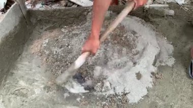 Kum ve çimentoyu çapayla karıştıran inşaat işçisinin 4K görüntüsü. Yakın açı, keskin doku, güçlü manuel çalışma havası. İnşaat, işçilik, sanayi, altyapı temaları için ideal.