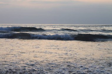 Gün batımında sakin okyanus dalgaları ve yumuşak pastel gökyüzü. Göz hizası açısı ve dalgalı suya odaklanma barışçıl ve rahatlatıcı bir ruh hali yaratır. Doğa, meditasyon, özgürlük, seyahat ve geçmiş kavramları için uygundur.