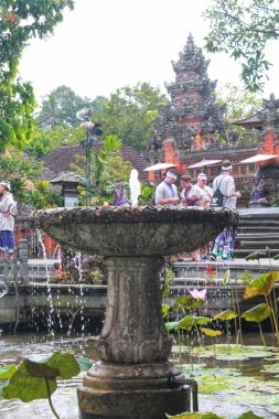 Pura Saraswati Tapınağı, Ubud, Bali 'deki nilüfer havuzunda yosunlu taş bir çeşme su sıçratır. Arka planda tapınak kıyafeti giymiş turistler var. Bu huzurlu, kültürel sahne seyahat ve miras teması için mükemmel. 11 Eylül 2024-Endonezya.