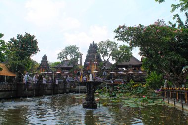 Ubud, Bali 'deki Saraswati Tapınağı' nın (Pura Taman Saraswati) geniş açılı manzarası. Süslü tapınak kapısı ve turistlere giden nilüferlerle dolu yemyeşil bir nilüfer havuzunda taştan bir çeşme bulunuyor. 11 Eylül 2024-Endonezya.