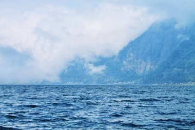Batur Dağı 'nın geniş açılı görüntüsü Bali Batur Gölü boyunca. Puslu volkanik tepeleri olan mavi su önplanı, yumuşak doğal ışık. Seyahat, doğa, peyzaj, arka plan tasarımı için harika.